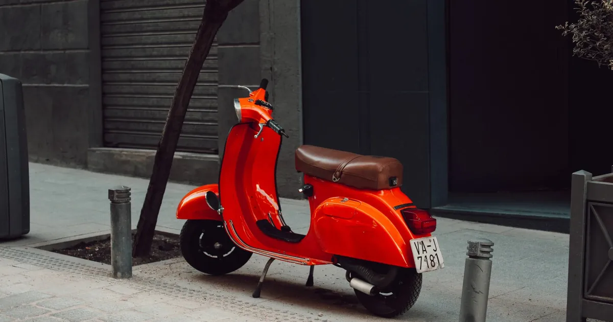 Coprigambe per scooter: Vespa rossa parcheggiata sul marciapiede in città